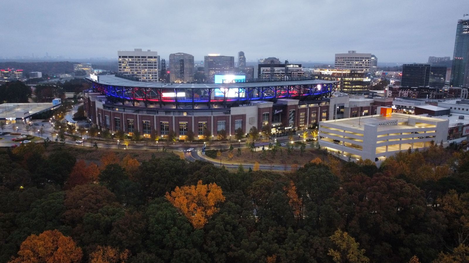 Truist Park lit up at dusk, seen from above with autumn trees in the foreground