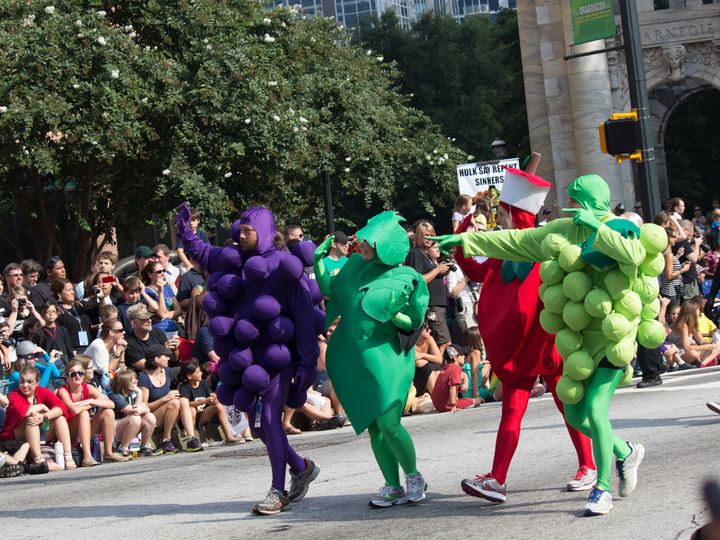 Parade walkers dressed as giant grapes and peas marching past a big crowd in downtown Atlanta
