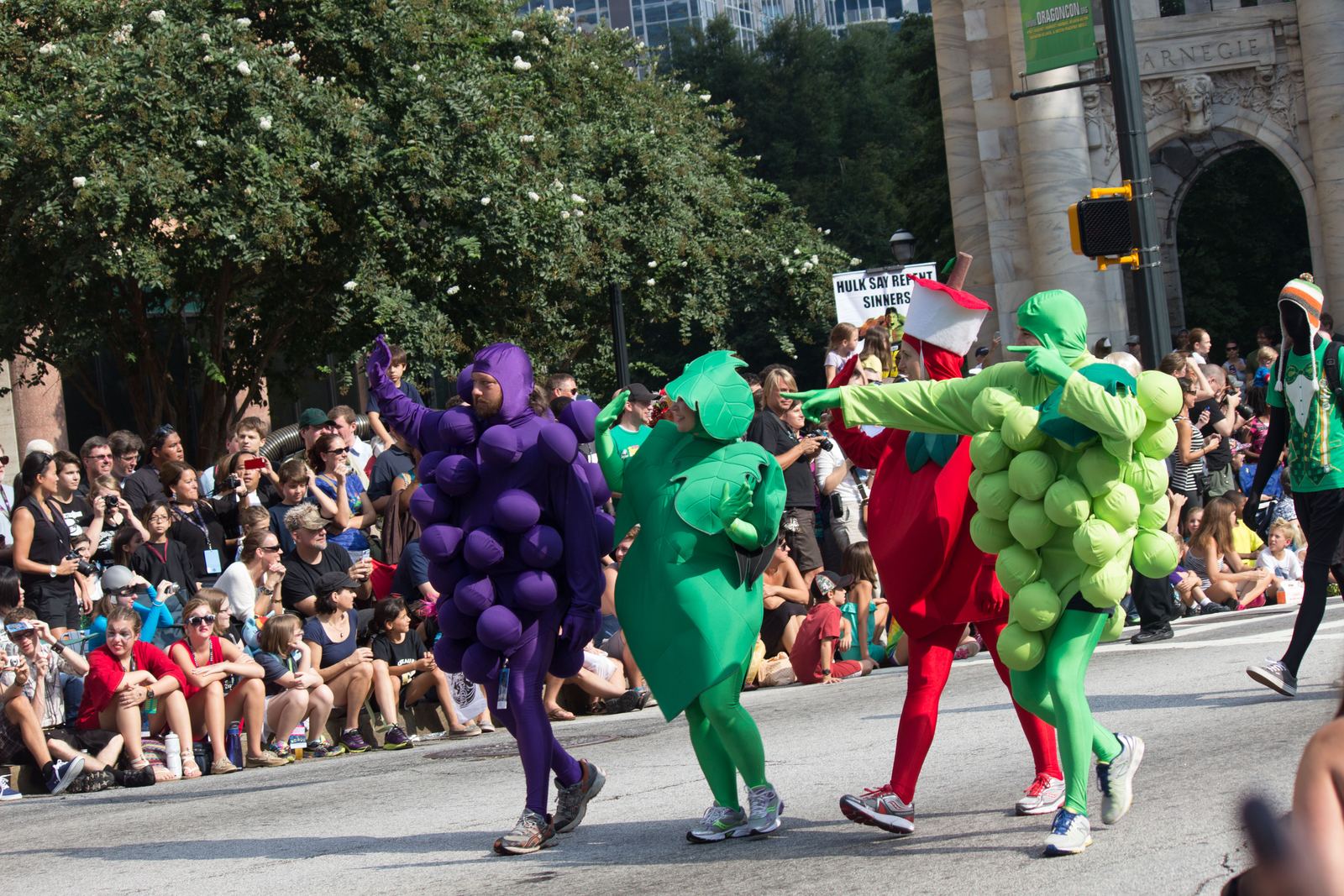 Parade walkers dressed as giant grapes and peas marching past a big crowd in downtown Atlanta