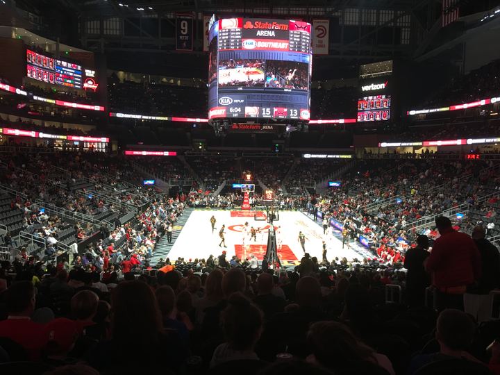 Crowd watching a Hawks home game inside State Farm Arena, with the scoreboard lit above the court