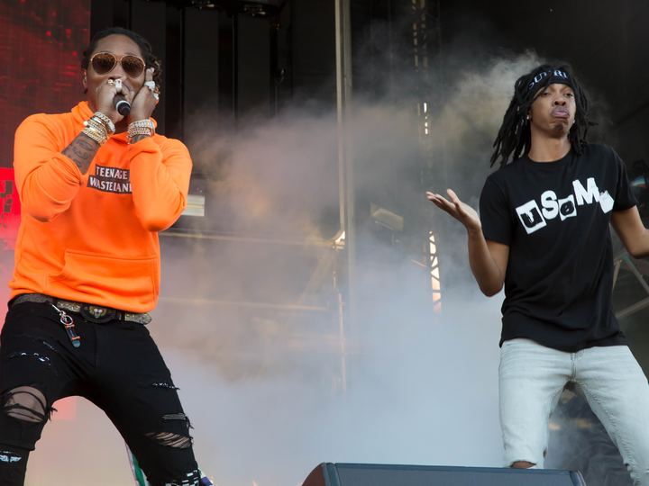 Atlanta rapper Future performing on an outdoor festival stage in an orange hoodie, with a hype man beside him in stage smoke