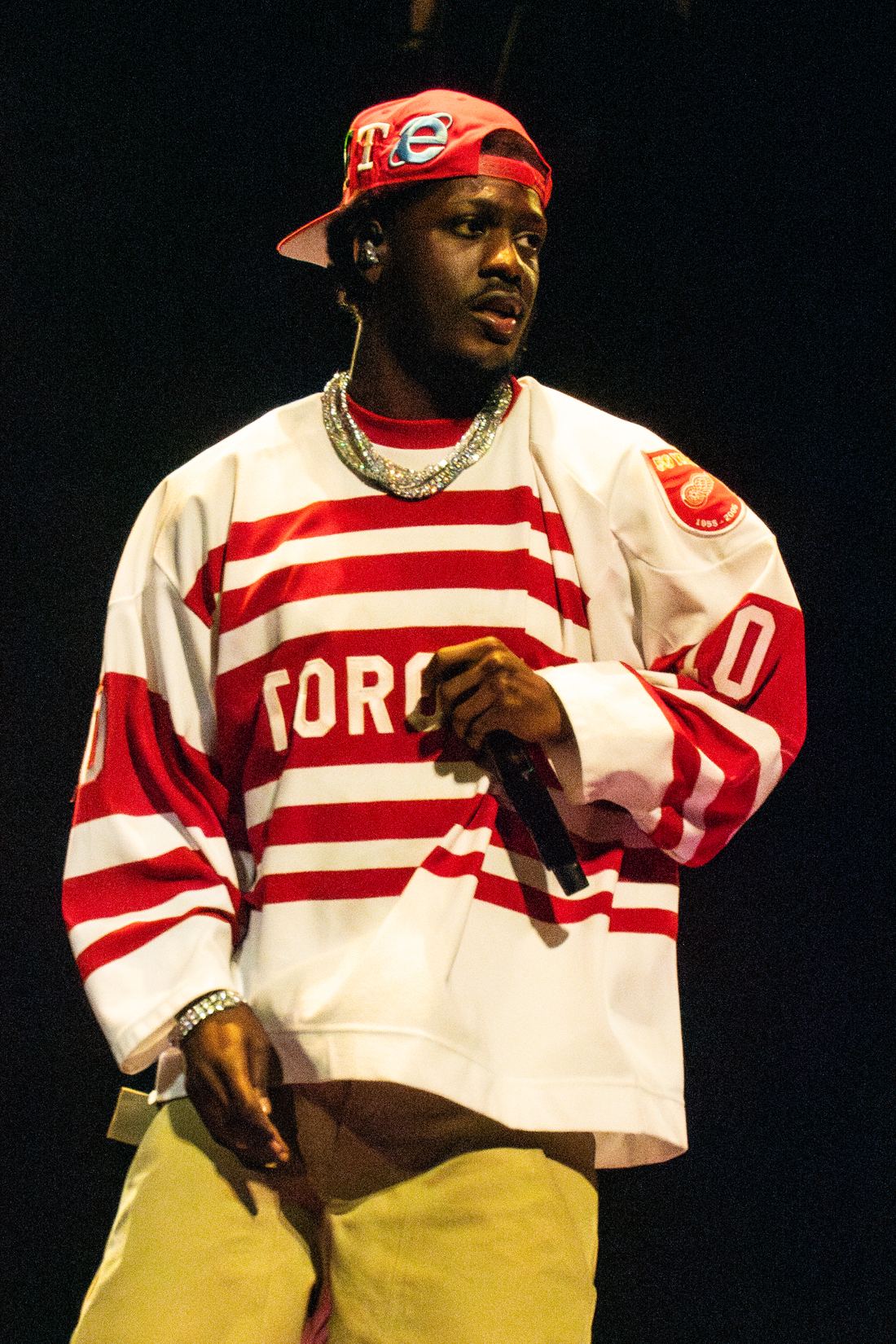Lil Yachty performing on stage with a microphone in a red and white jersey