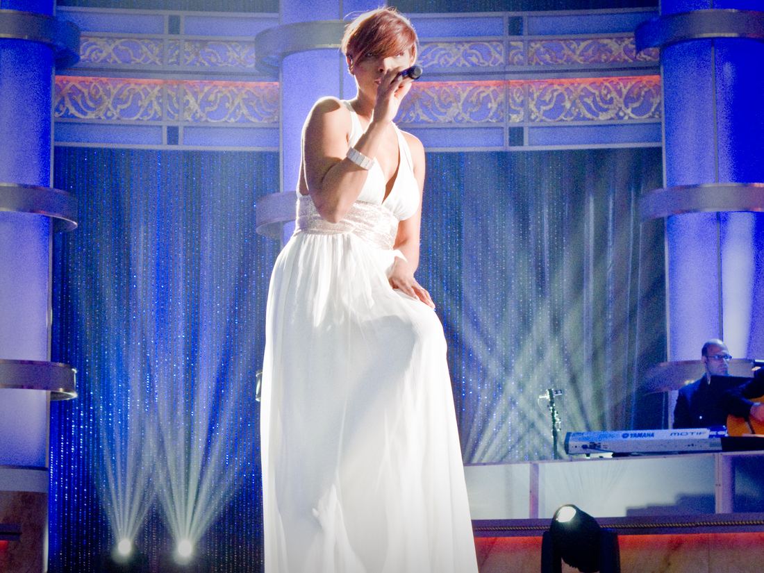 Toni Braxton singing in a white gown on a blue-lit stage
