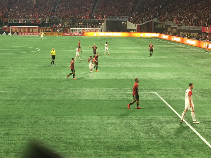 Atlanta United players in red and black stripes on the pitch at Mercedes-Benz Stadium during a 2018 match