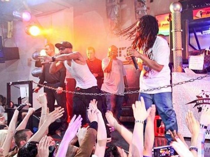 Lil Jon and his crew performing on a club stage above a crowd with raised hands