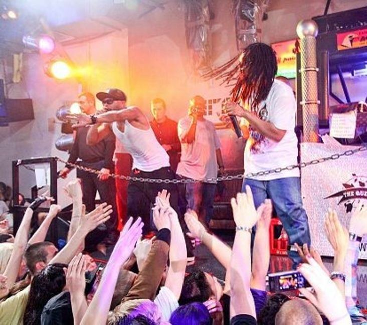 Lil Jon and his crew performing on a club stage above a crowd with raised hands