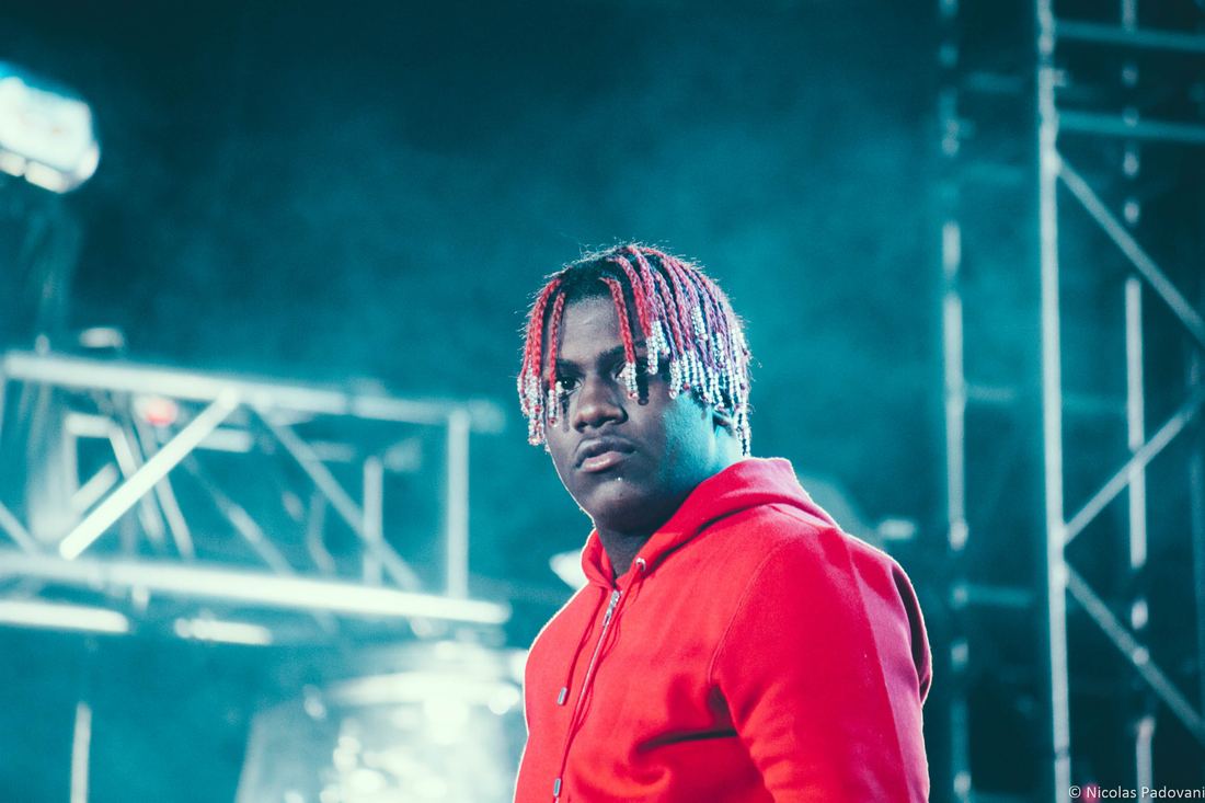 Lil Yachty with his signature red braids and a red hoodie on a festival stage
